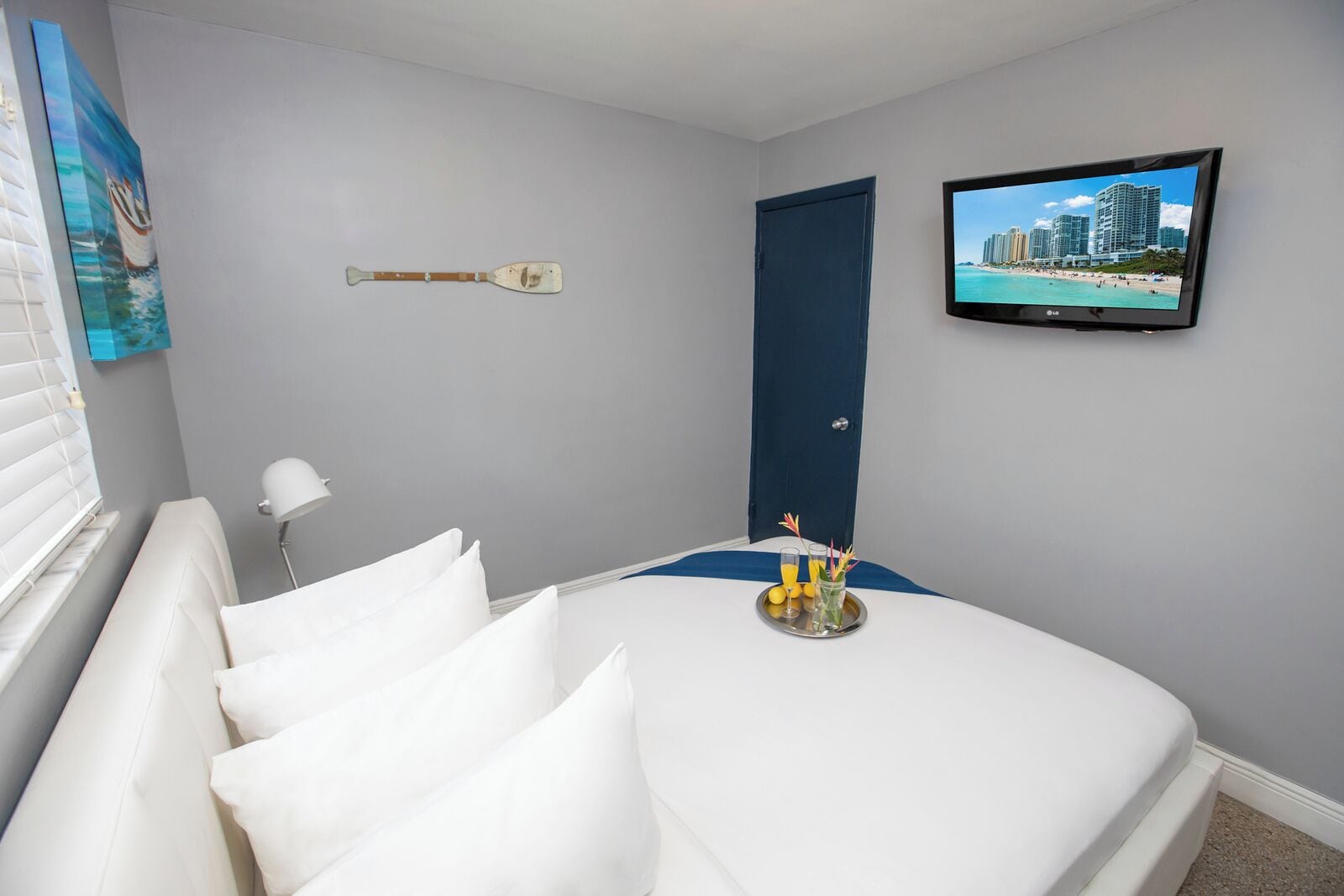 A hotel room with a bed, a television, a painting, and a door.