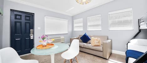 A modern living room with a glass table, white chairs, a beige sofa, and a black door.
