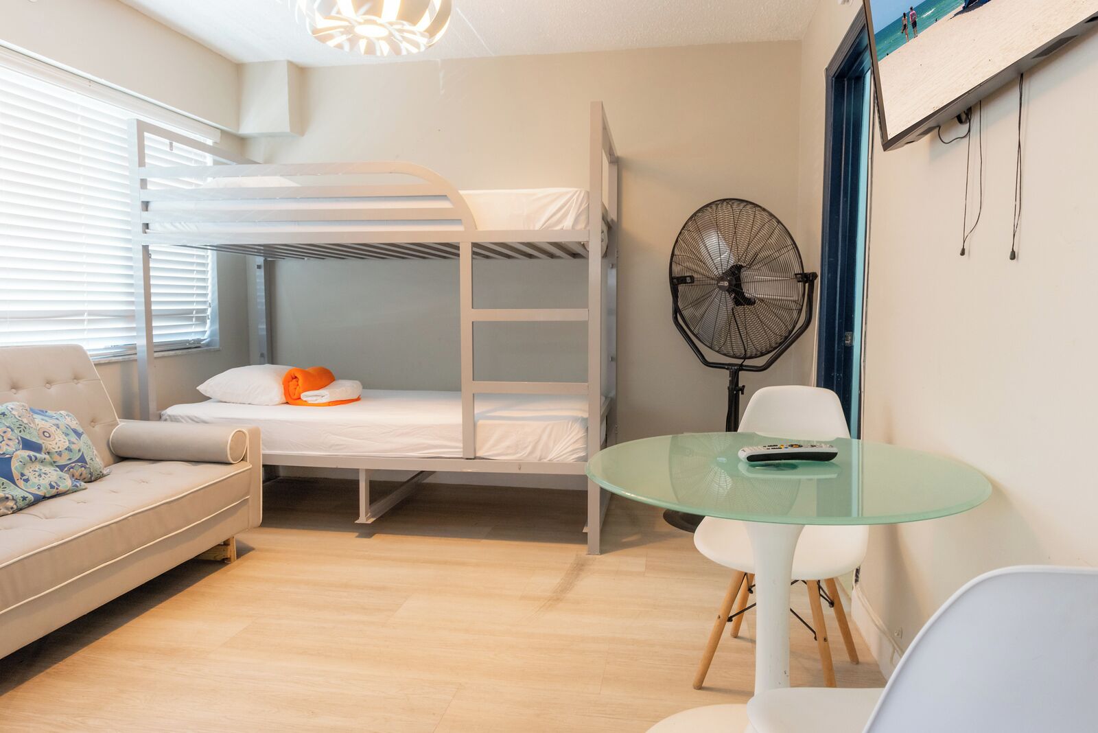 A bunk bed room with a sofa, a glass table, and a fan.
