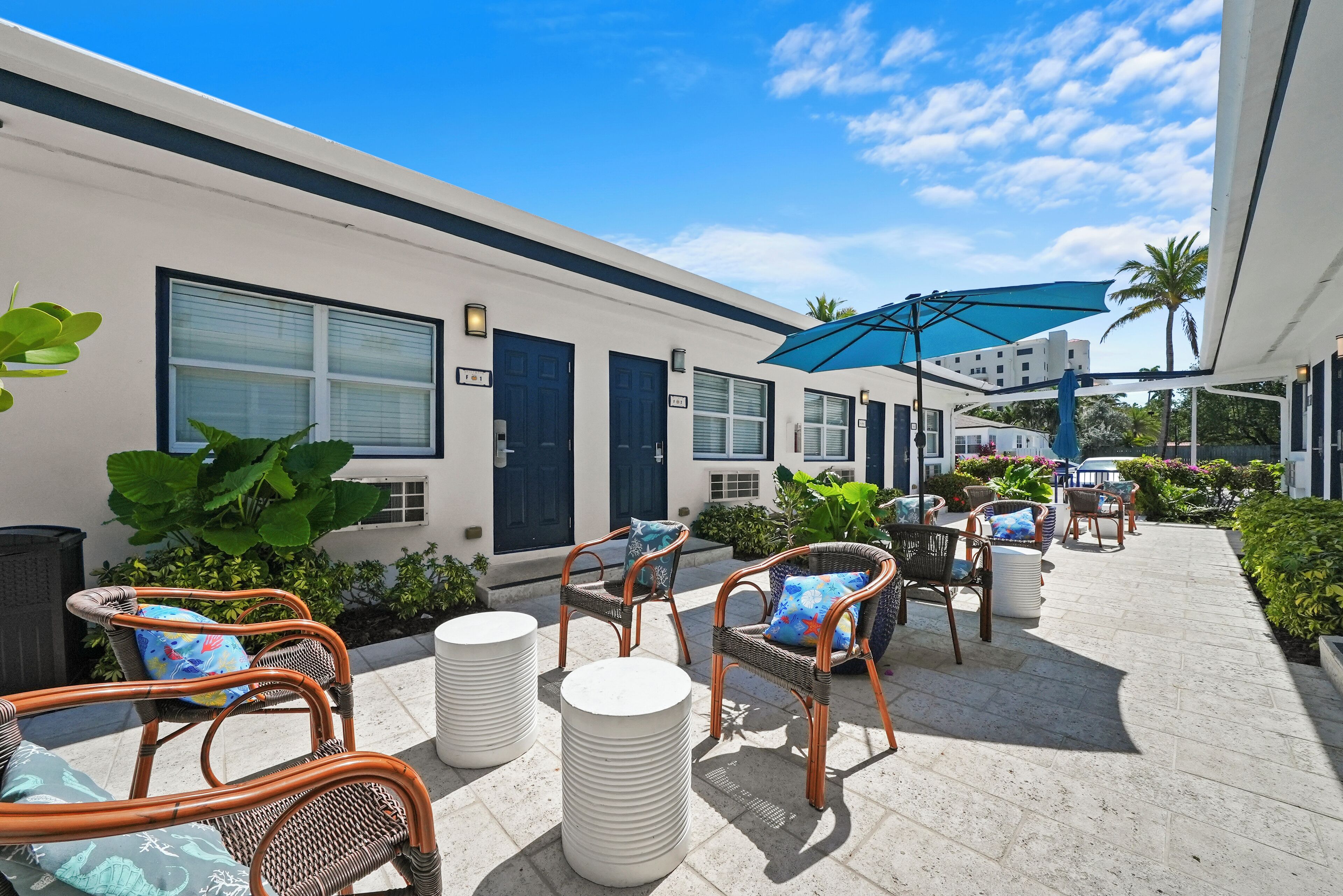 A hotel patio with wicker furniture, a blue umbrella, and a white building facade.