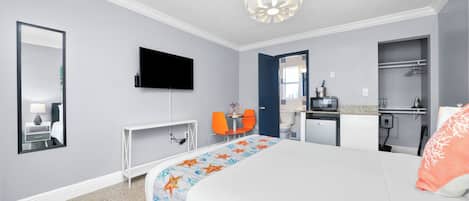 Habitación de hotel moderna con cama, escritorio, silla, televisor y kitchenette.