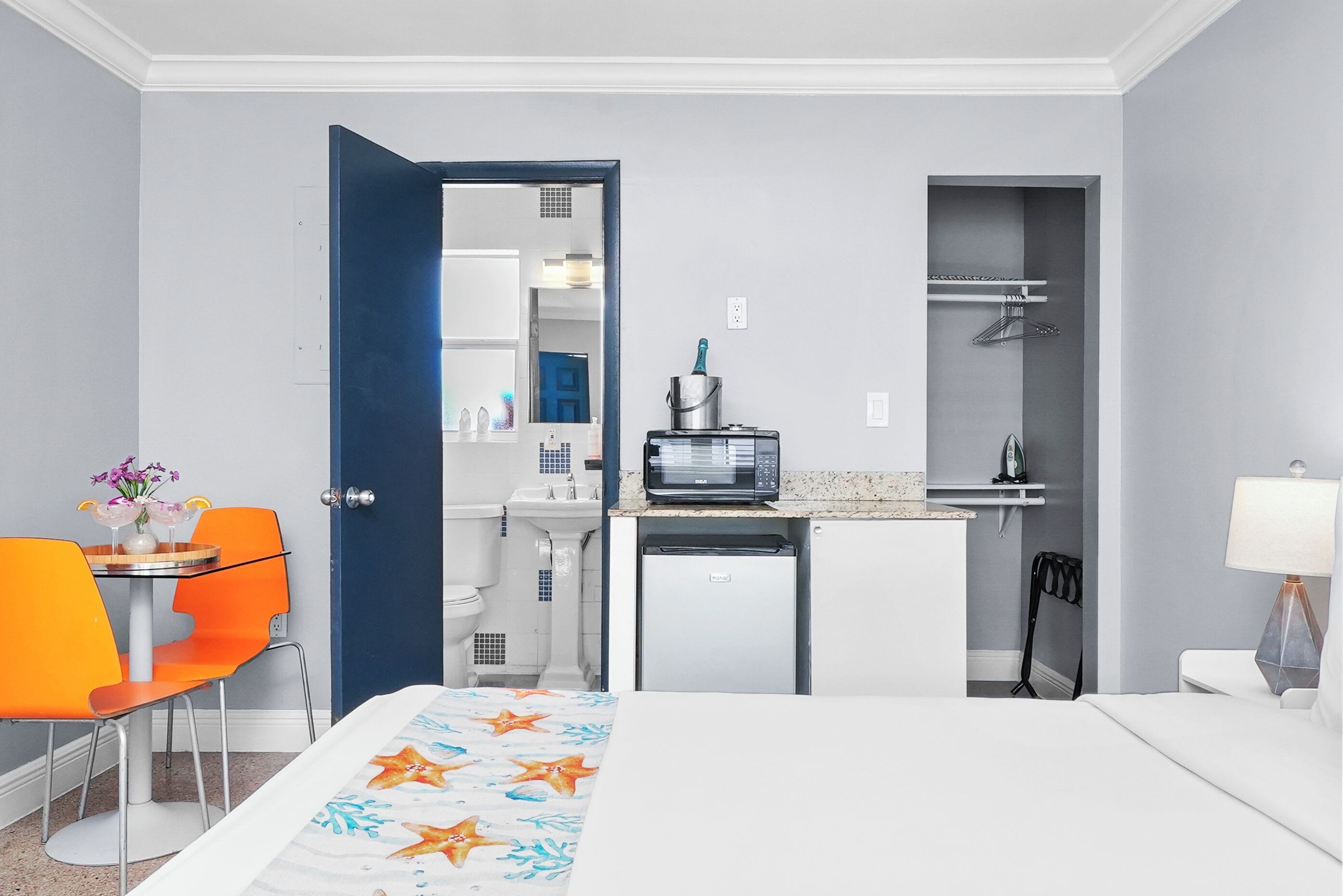 A hotel room with a bed, a small kitchenette, a bathroom, and a dining area with a table and chairs.