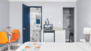 A hotel room with a bed, a small kitchenette, a bathroom, and a dining area with a table and chairs.