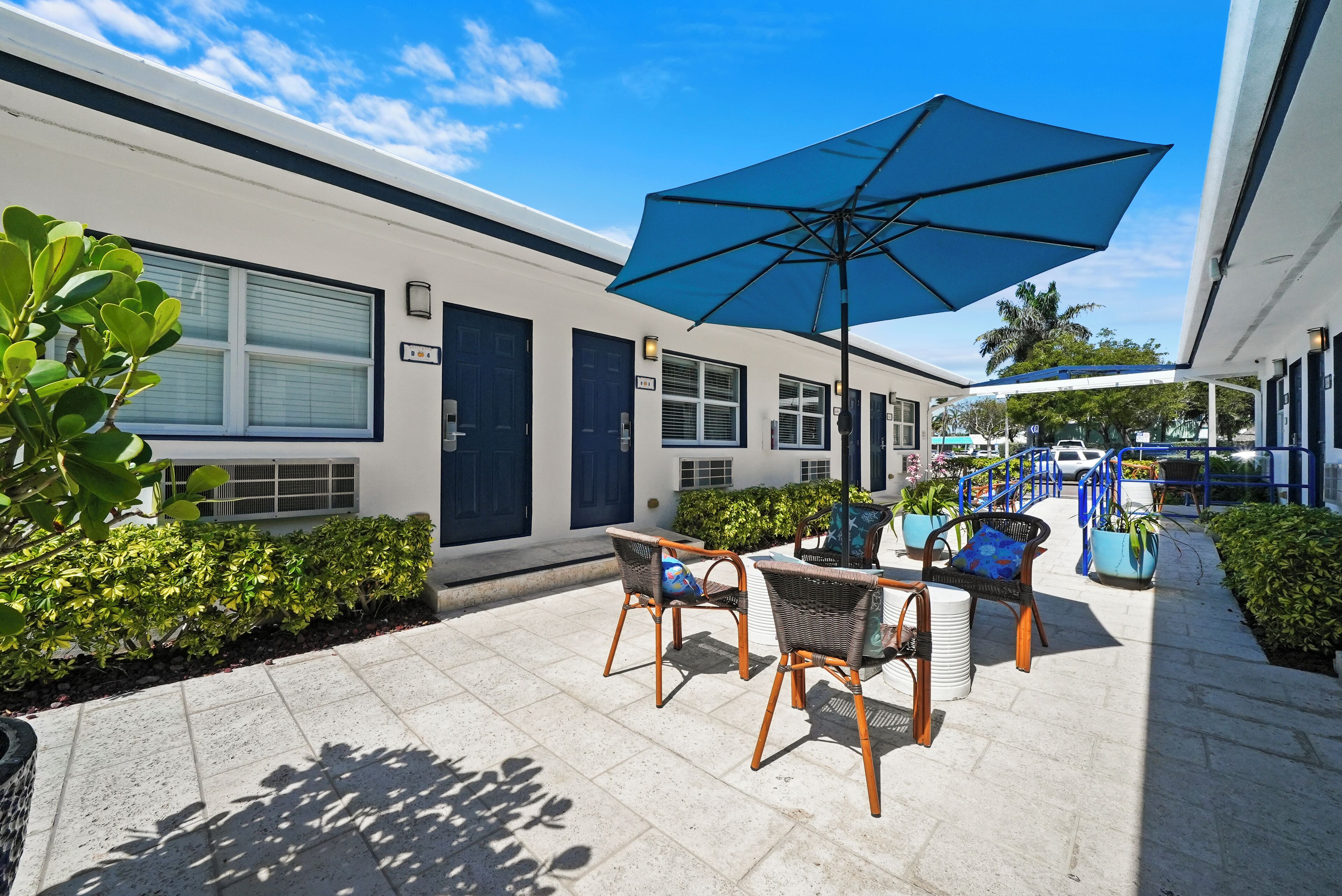 En pæn, moderne udendørs terrasse med fletmøbler og en stor blå parasol.
