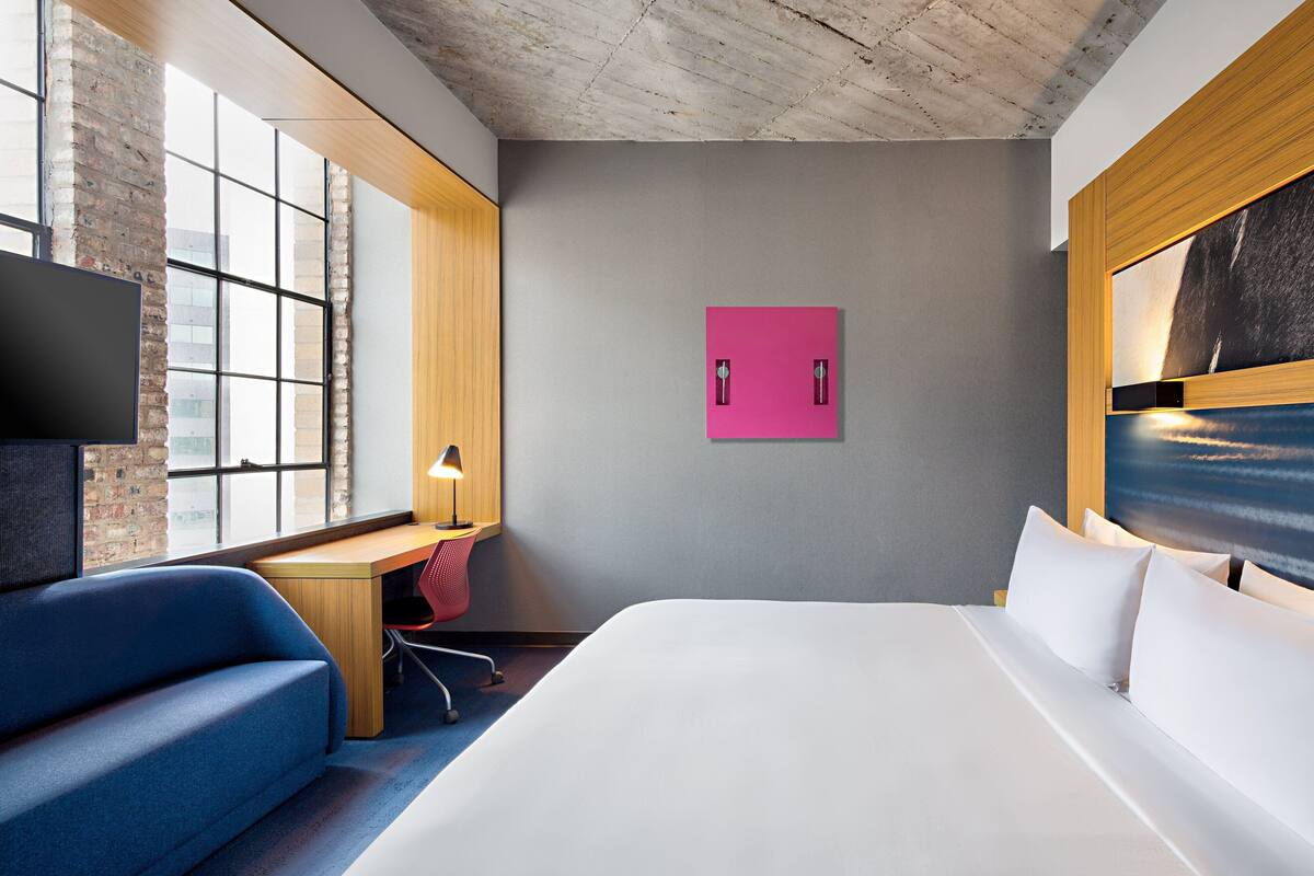 A modern hotel room with a large bed, a desk, a blue sofa, and a TV.