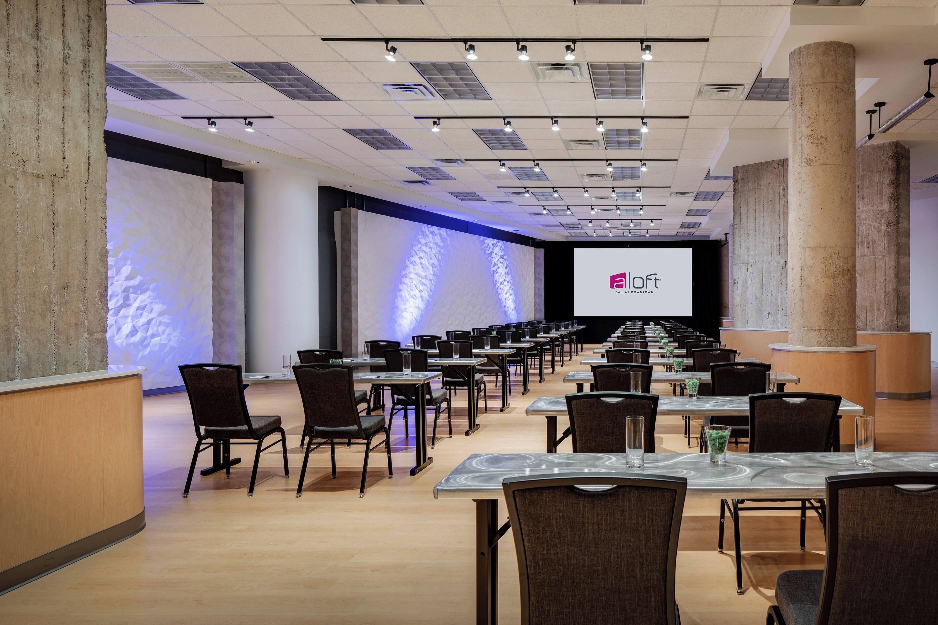 A conference room with rows of tables and chairs, a large screen, and a stage.