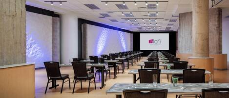 A conference room with rows of tables and chairs, a large screen, and a stage.