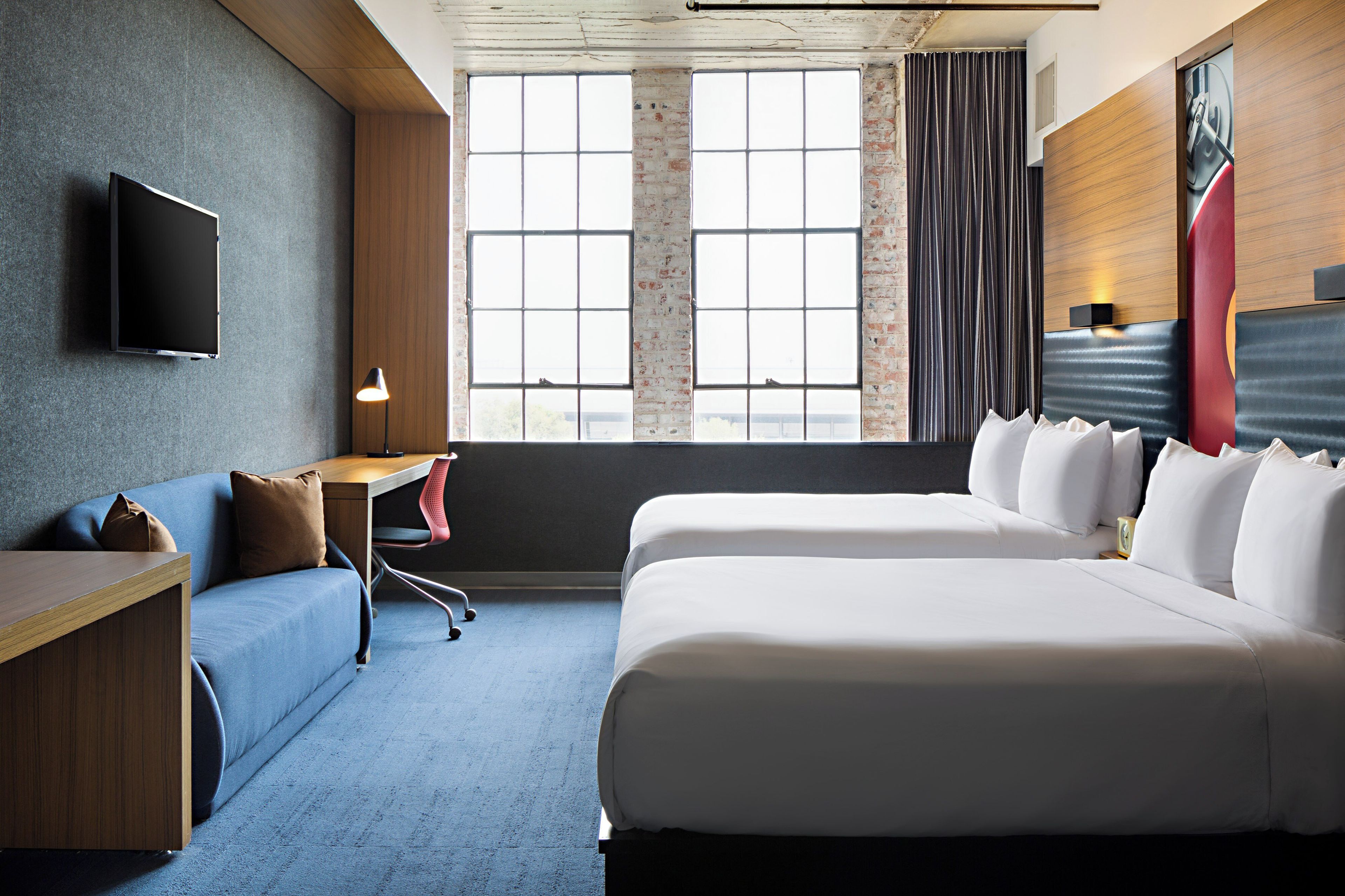 A hotel room with a bed, a desk, a chair, a TV, and a large window with curtains.