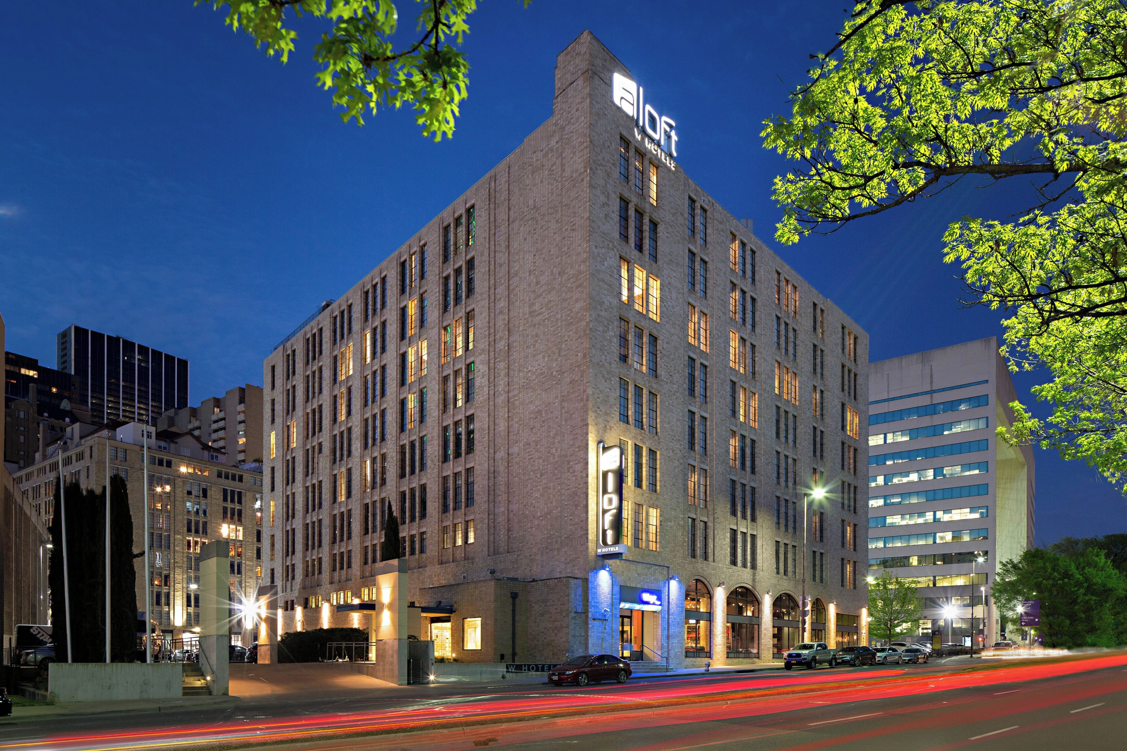 A multi-story hotel with a prominent 'Aloft' sign, featuring a classic architectural style with a flat roof and large windows.