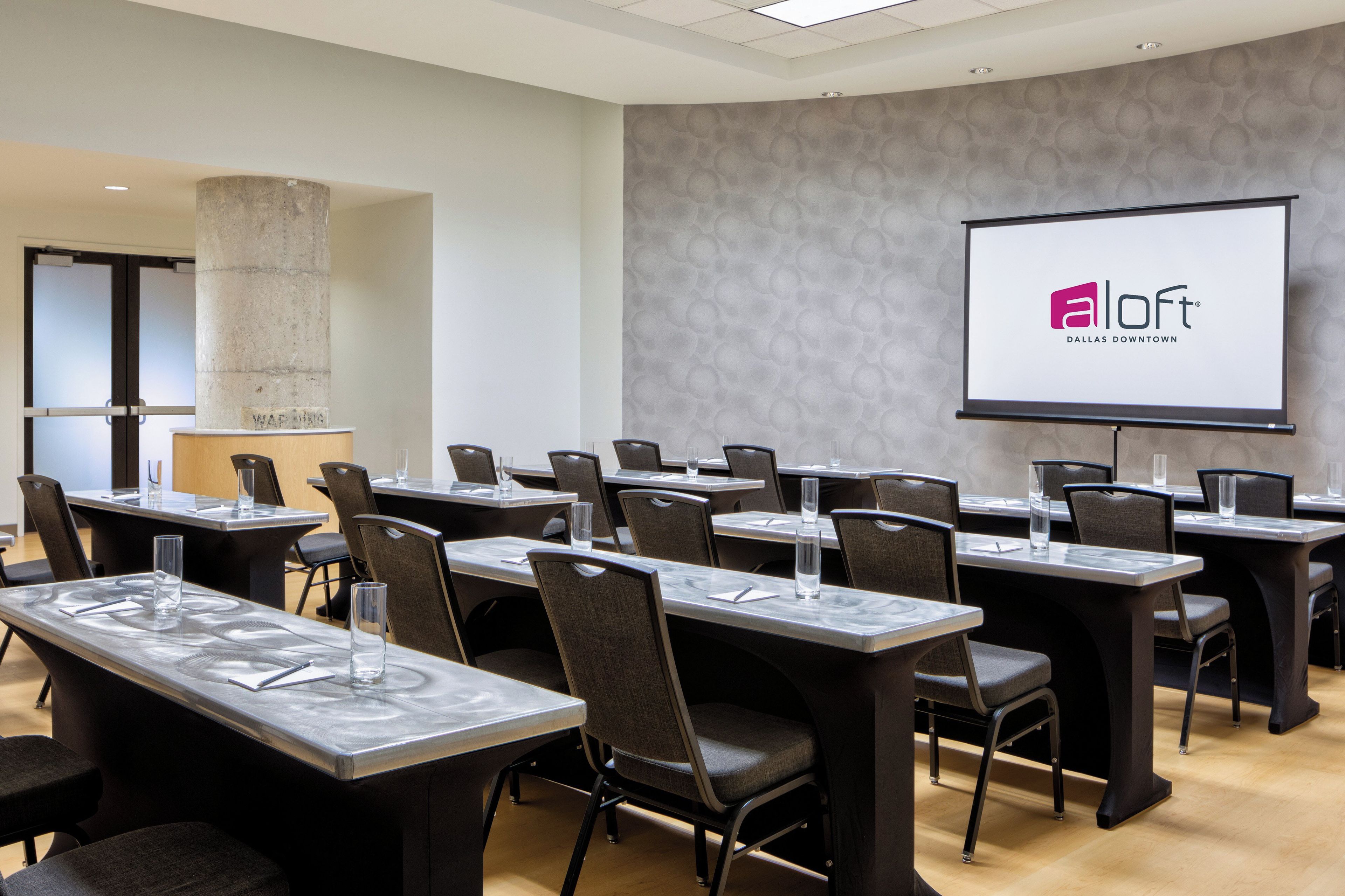 A conference room with tables, chairs, and a projection screen displaying a logo.