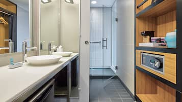 A modern bathroom with a double sink, a glass shower enclosure, and a control panel on the wall.