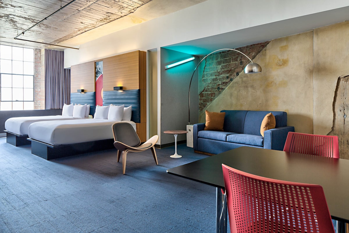 Una habitación de hotel moderna con una cama grande, un sofá, una mesa de comedor y una mesita.