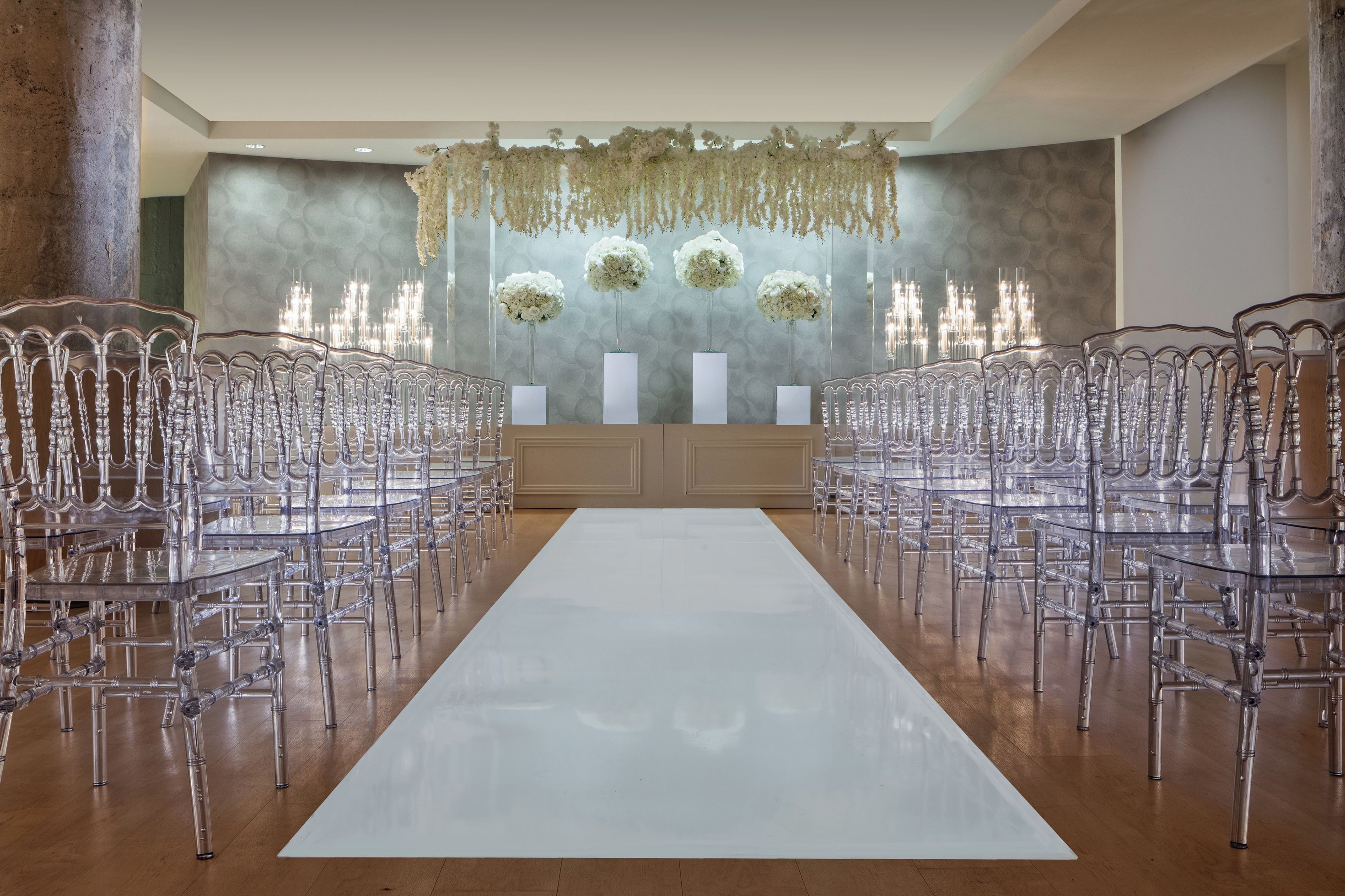 A wedding ceremony setup with clear chairs and a white aisle.