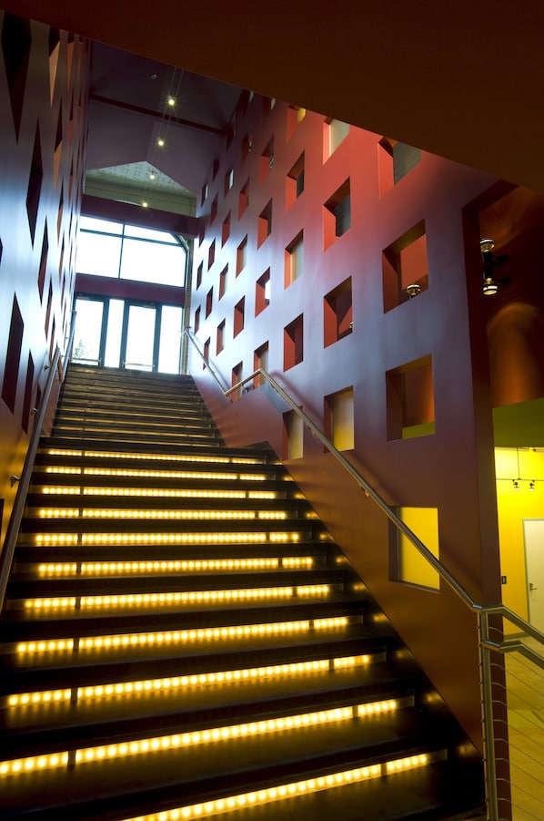 Een trap met verlichte treden die naar een hoger niveau leidt, omgeven door muren met geometrische uitsneden en een leuning aan de rechterkant.