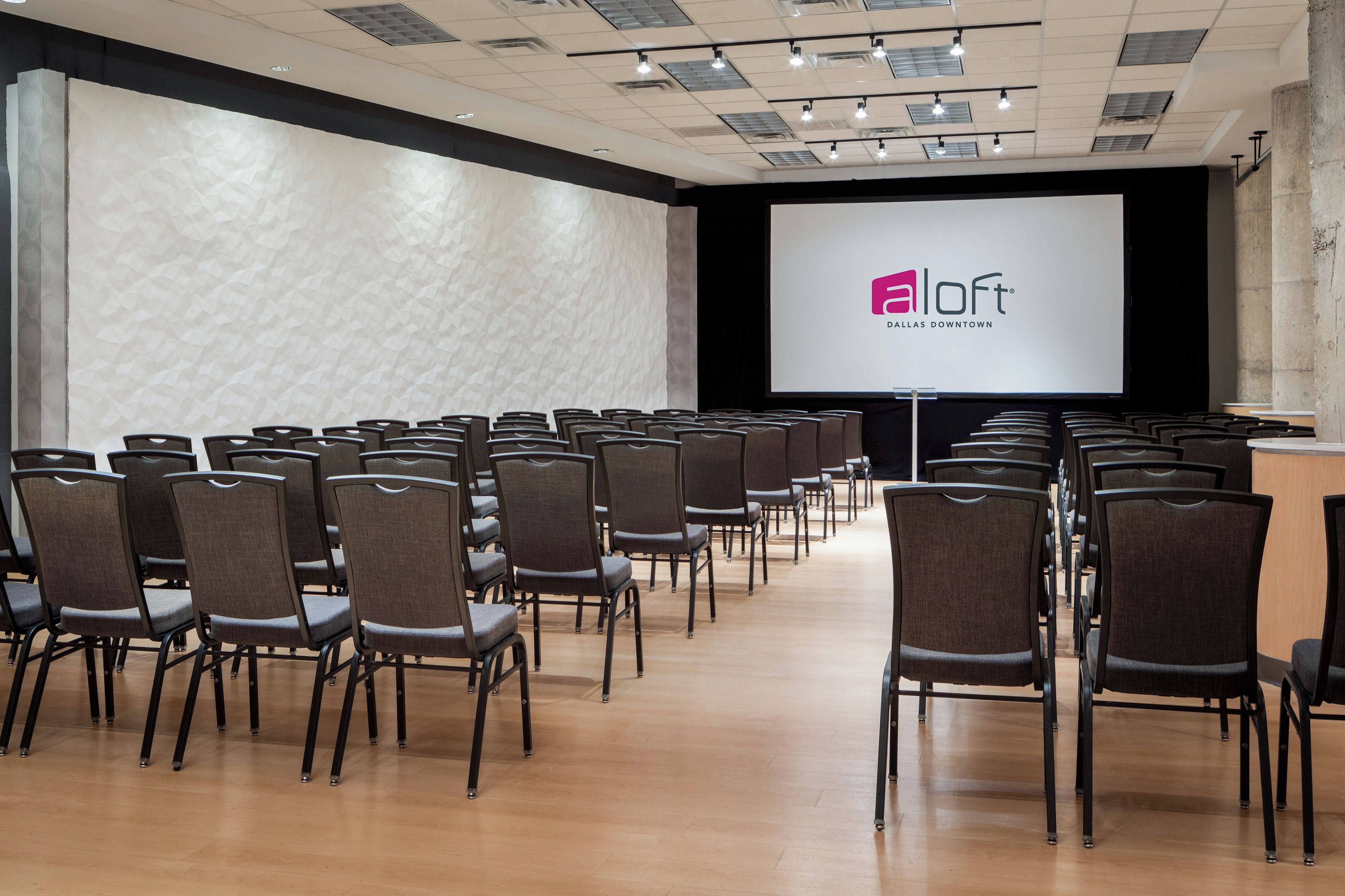 A conference room with rows of chairs, a projection screen, and a stage area.
