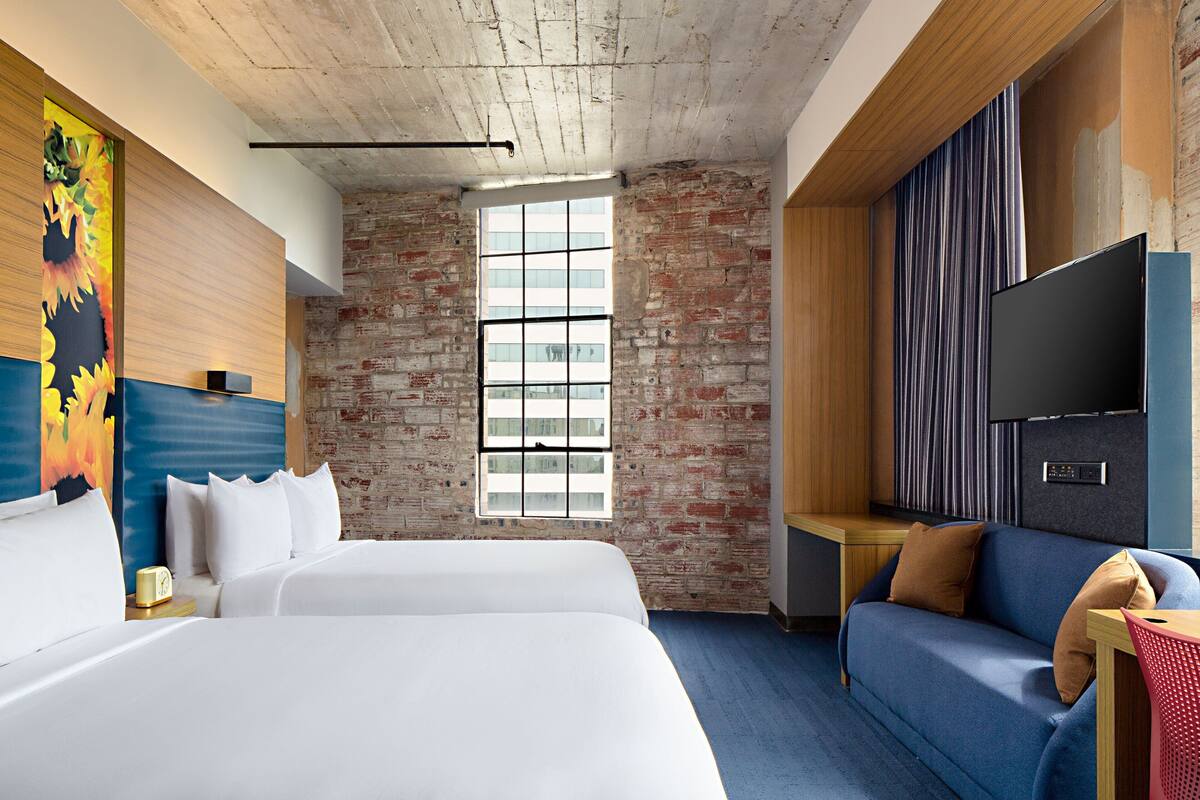 A hotel room with a large bed, a sofa, a TV, and a brick wall.