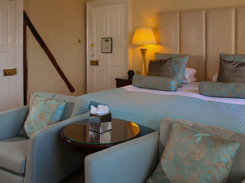 A hotel room with a bed, two armchairs, a small table with a tissue box, a lamp, and a door.