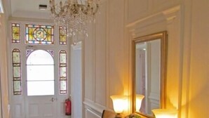 A hallway with a chandelier, stained glass windows, a fire extinguisher, and a table with flowers and lamps. - Cley Hall Hotel (Spalding)