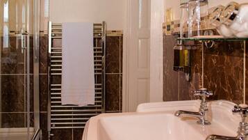 Un bagno con box doccia in vetro, un asciugamano bianco su un porta asciugamani e uno scaffale in vetro con articoli da toilette.