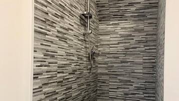 Une douche au design moderne, dotée d’un mur texturé et d’un pommeau de douche à main.