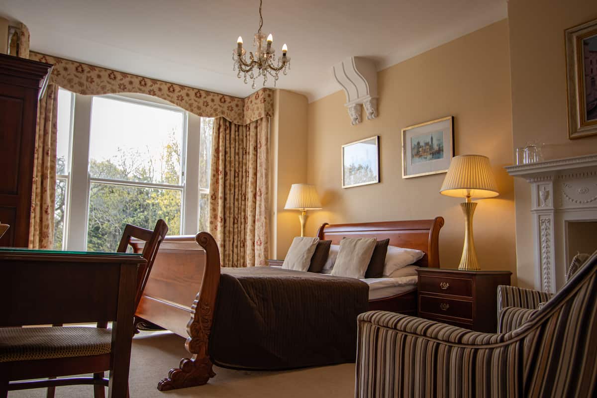 A hotel room with a bed, two bedside lamps, a fireplace, a desk, and a chair.