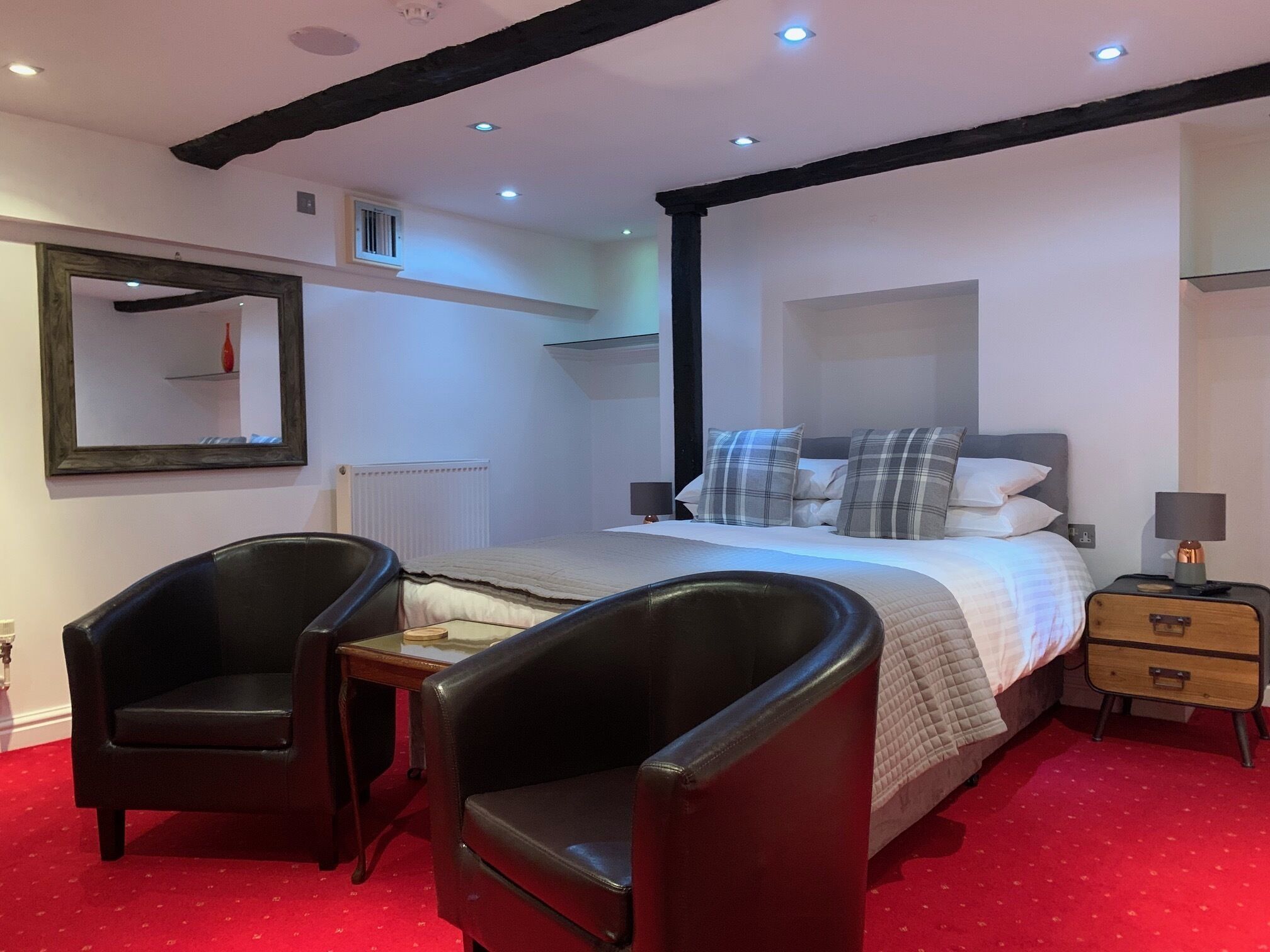Un dormitorio con una cama, dos sillas, una mesita de noche, una lámpara y un espejo.