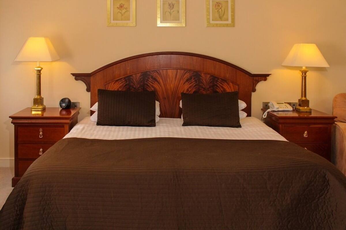 A neatly made bed with a wooden headboard, two bedside tables with lamps, and three framed floral pictures on the wall.