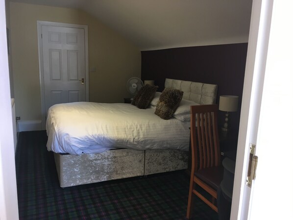 Un dormitorio con cama, una silla, un ventilador y una puerta.