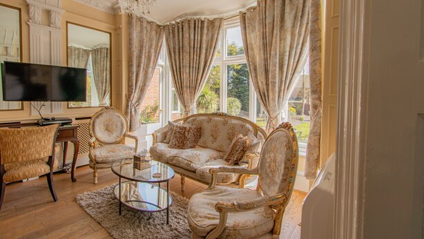 A spacious living room with a large window, elegant furniture, and a flat-screen TV. - Cley Hall Hotel (Spalding)