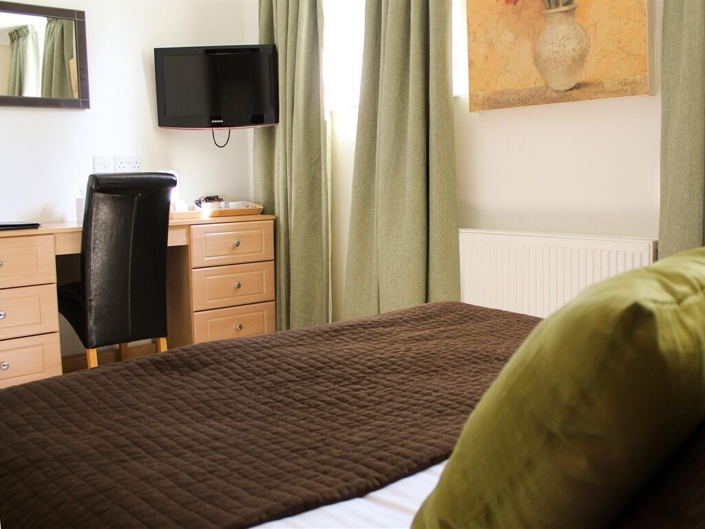 Una habitación de hotel con cama, escritorio, silla, televisión y un cuadro en la pared.