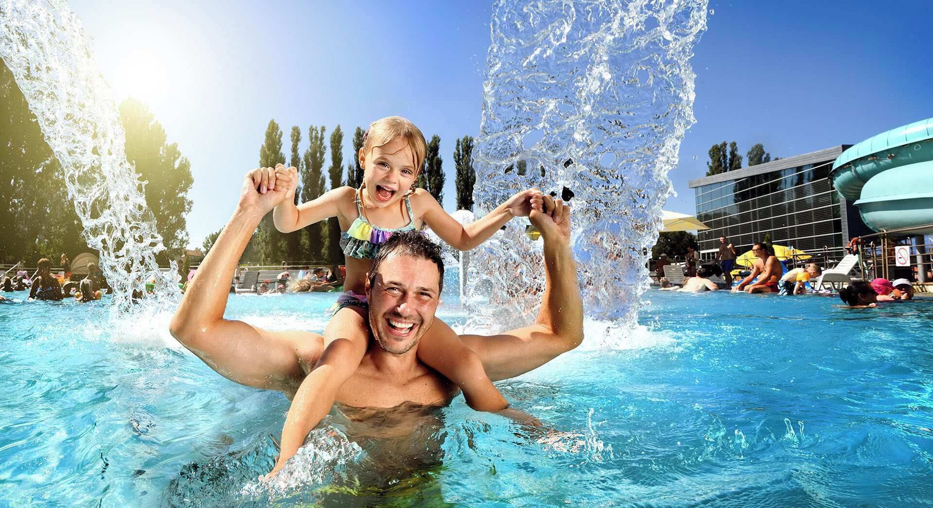 A man carrying a child in a swimming pool with water jets.