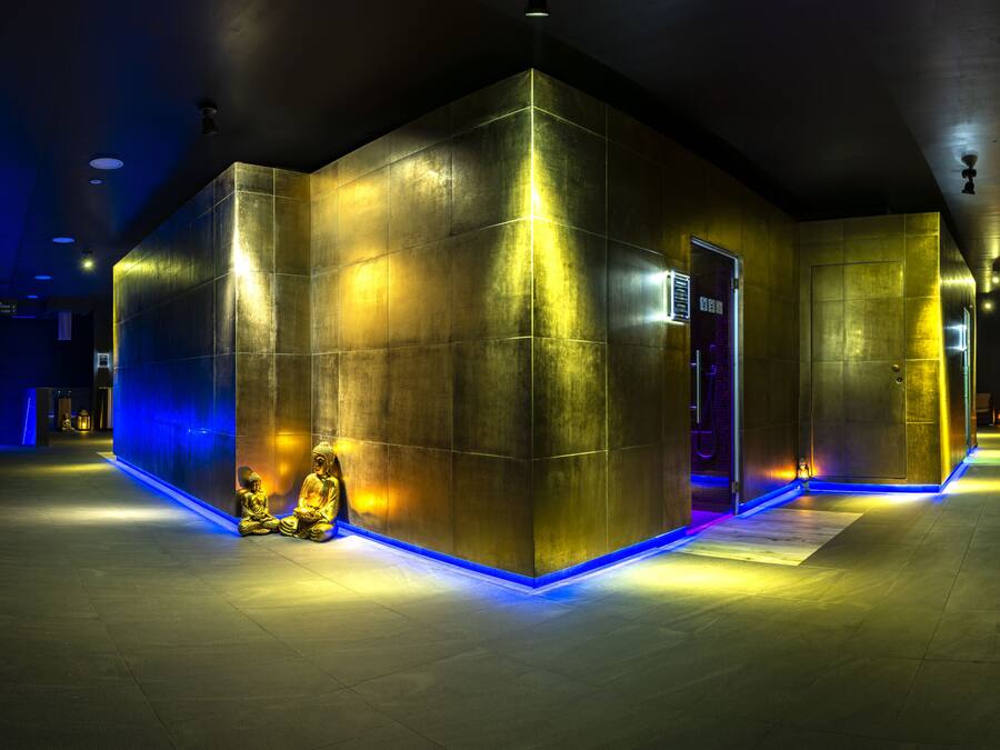 A modern interior with a geometric design, featuring a reception area with a blue-lit pathway and golden statues.