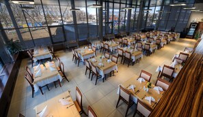 Ein geräumiges Restaurant mit mehreren Tischen und Stühlen, große Fenster mit Blick auf den Parkplatz und umliegende Gebäude.