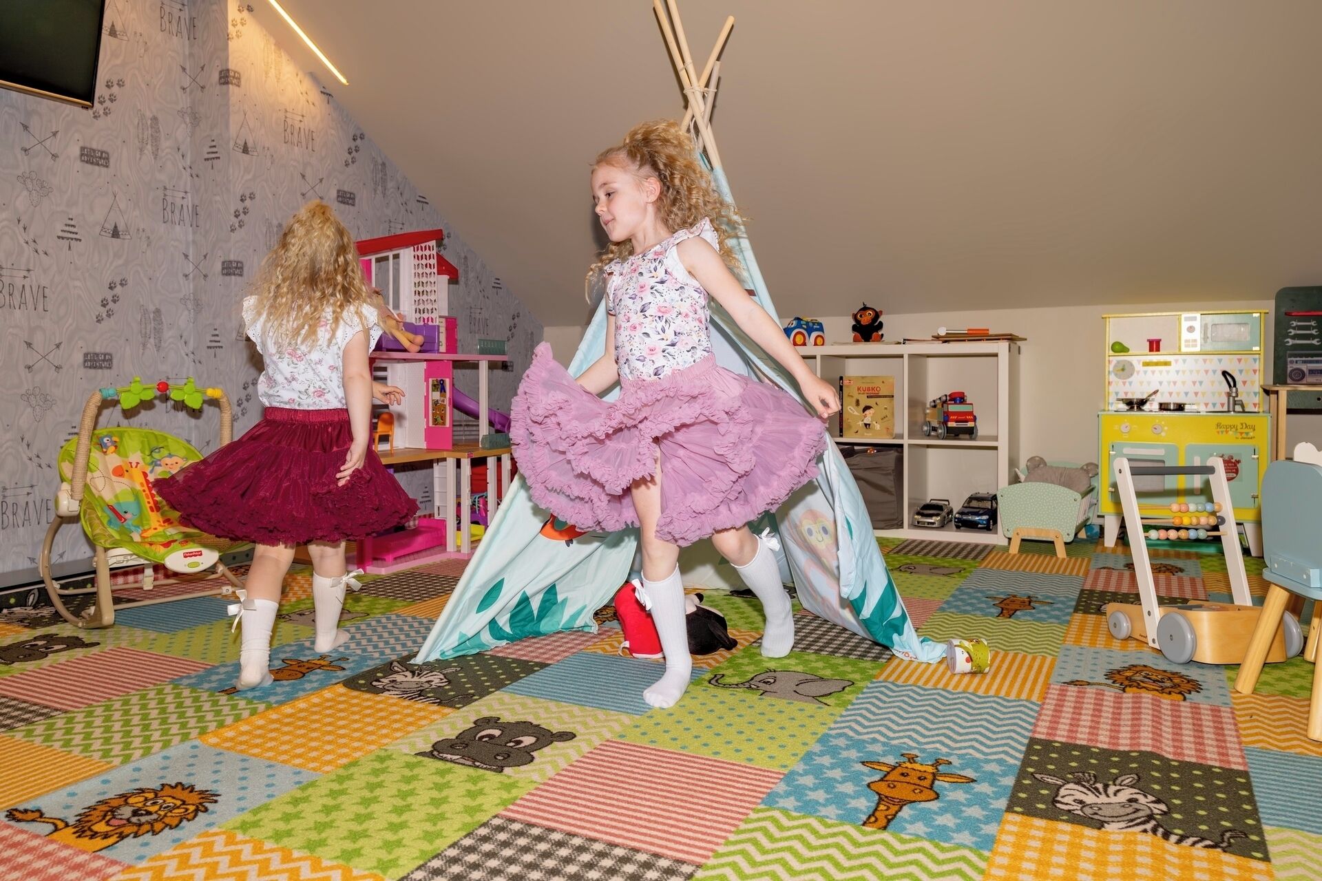 Two children playing in a room with a colorful floor, a playhouse, and various toys.