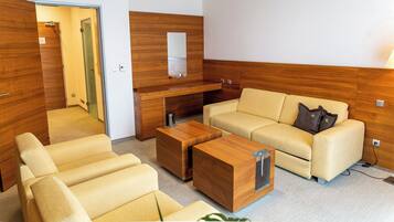 Habitación de hotel moderna con sofá, dos sillones, una mesita de centro de madera, un escritorio con espejo y una lámpara.