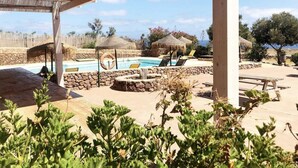 Un área de piscina con sillones reclinables, una chimenea de piedra y una pérgola.