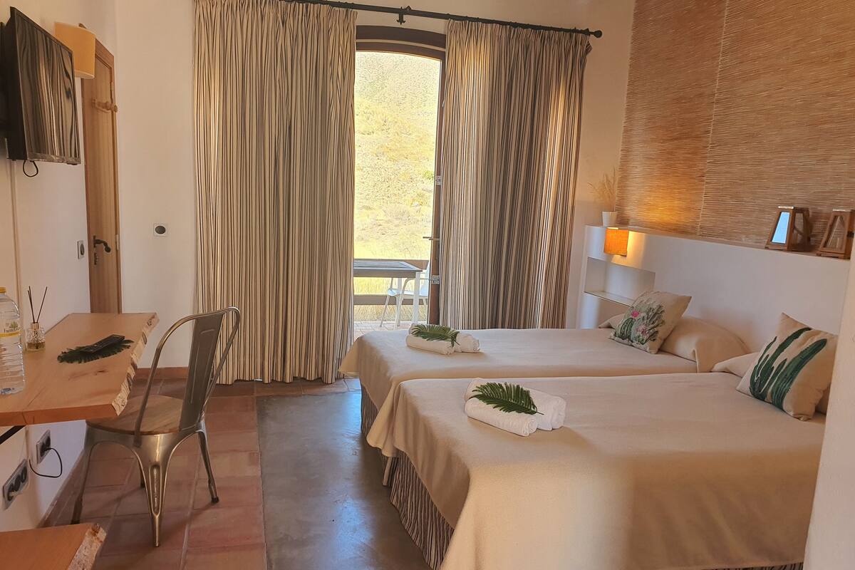 A hotel room with a bed, a desk, a chair, and a window with curtains.