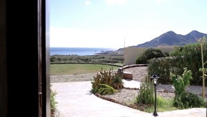 Vista desde una ventana que da a un jardín con un cactus, un farol y una cadena montañosa distante.