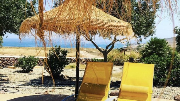 Dos sillones amarillos bajo un sombrilla de paja, con vista a la playa y el océano.