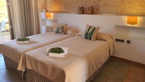 Habitación de hotel con dos camas, cada una con una almohada y una toalla. Hay lámparas de pared y una mesita con una lámpara.