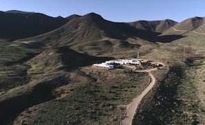 Un complejo de edificios blancos y aislados, con varias construcciones, rodeado de terreno montañoso y accidentado.