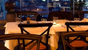 Mesa de restaurante posta com toalhas brancas, copos e talheres.