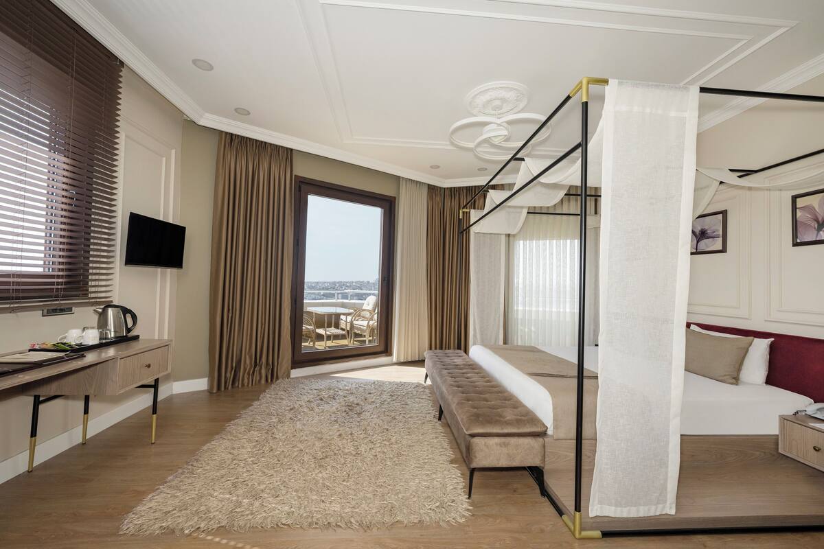 Une chambre d’hôtel moderne dotée d’un grand lit, d’un bureau avec un téléviseur à écran plat, d’un banc et d’un balcon offrant une vue sur la ville.