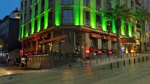 Hotel de vários andares com design moderno, apresentando varandas e entrada de canto com área de estar externa.