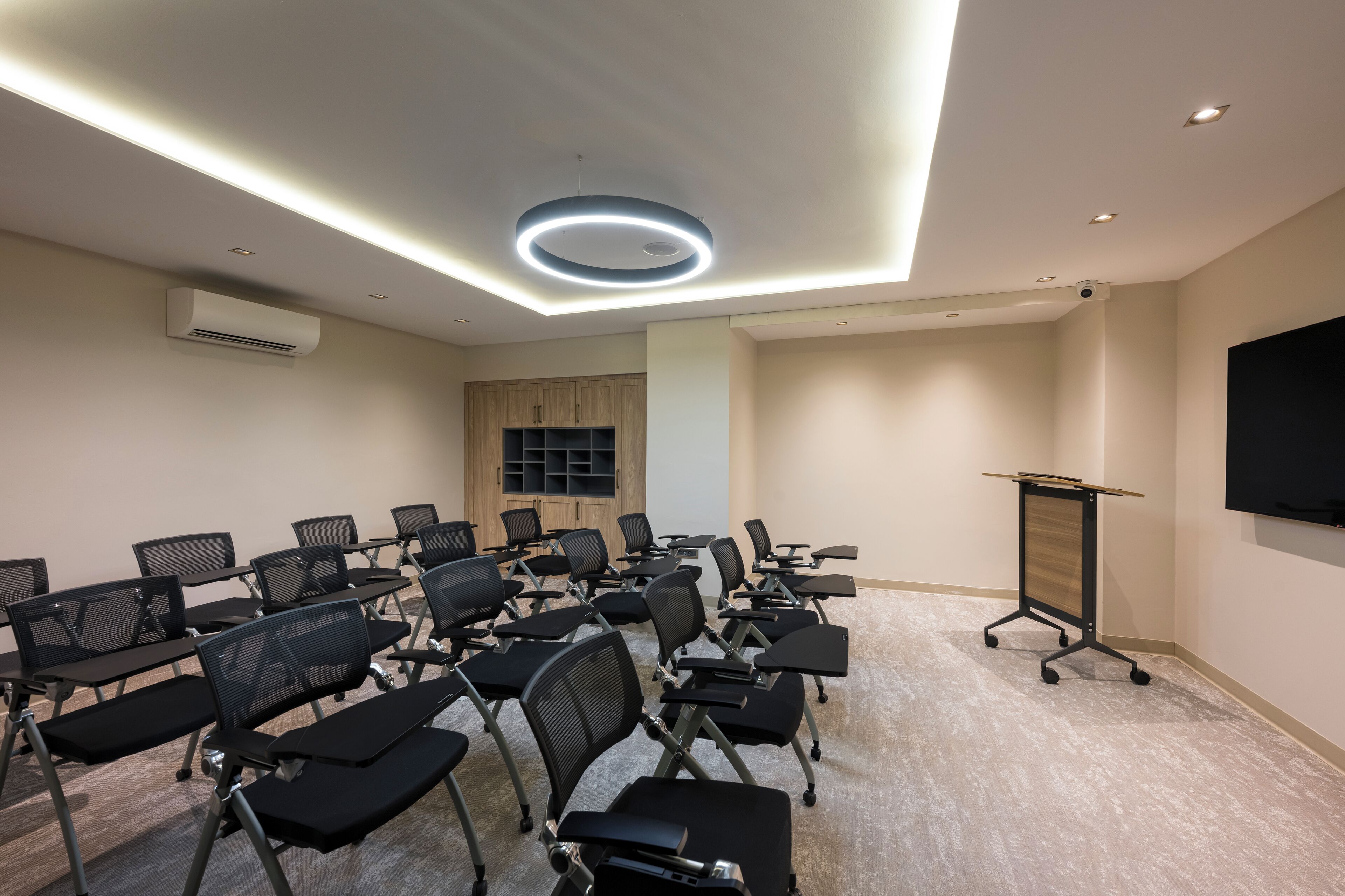 A conference room with rows of black chairs, a podium, and a flat-screen TV on the wall.