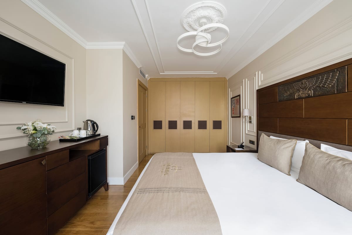Une chambre d’hôtel dotée d’un grand lit, d’un téléviseur à écran plat fixé au mur, d’une commode en bois et d’un luminaire moderne au plafond.
