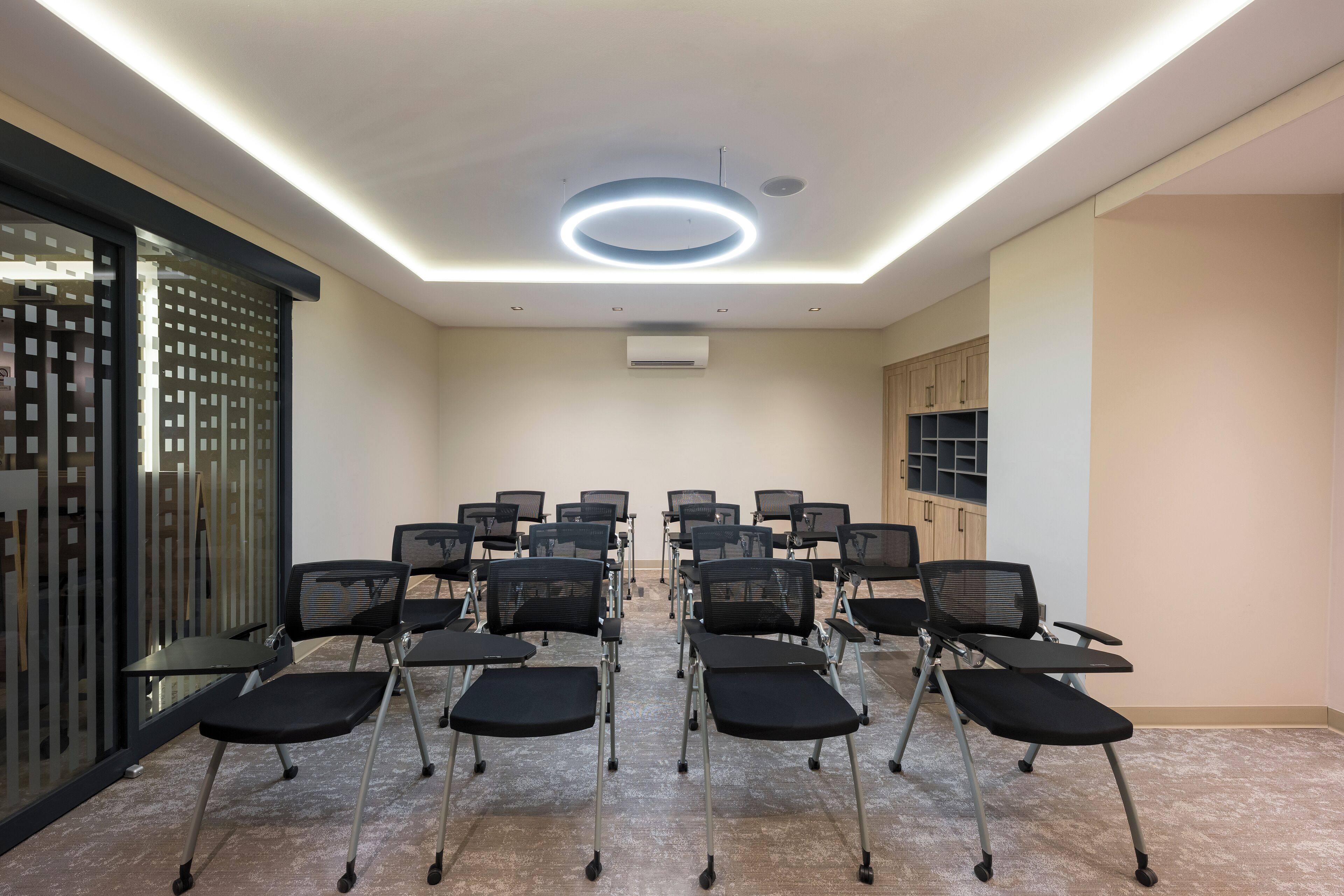 A conference room with rows of black chairs, a ceiling light, and a wall-mounted air conditioner.