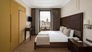 Quarto de hotel com uma cama grande, uma mesinha de cabeceira com abajur, uma TV e vista para a cidade através de uma janela.