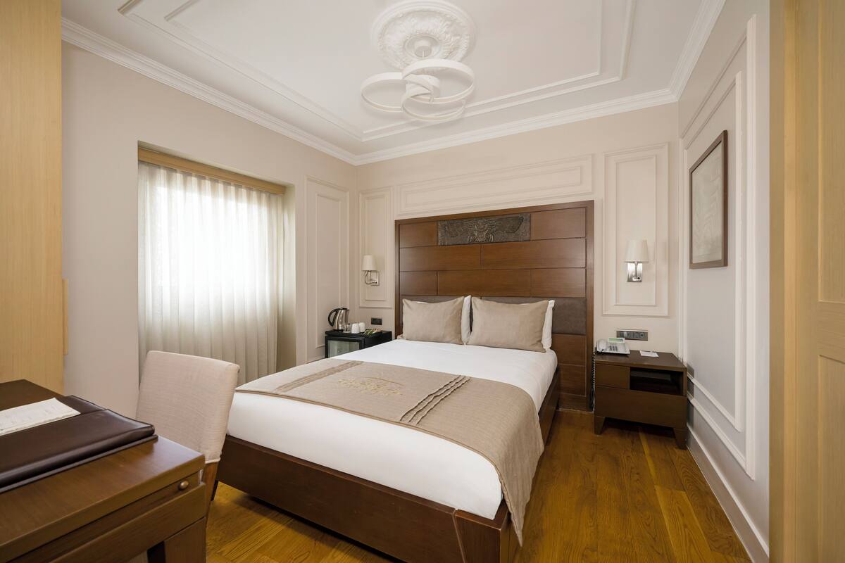 Une chambre d’hôtel avec un grand lit, un bureau, une chaise, une table de chevet et une lampe.
