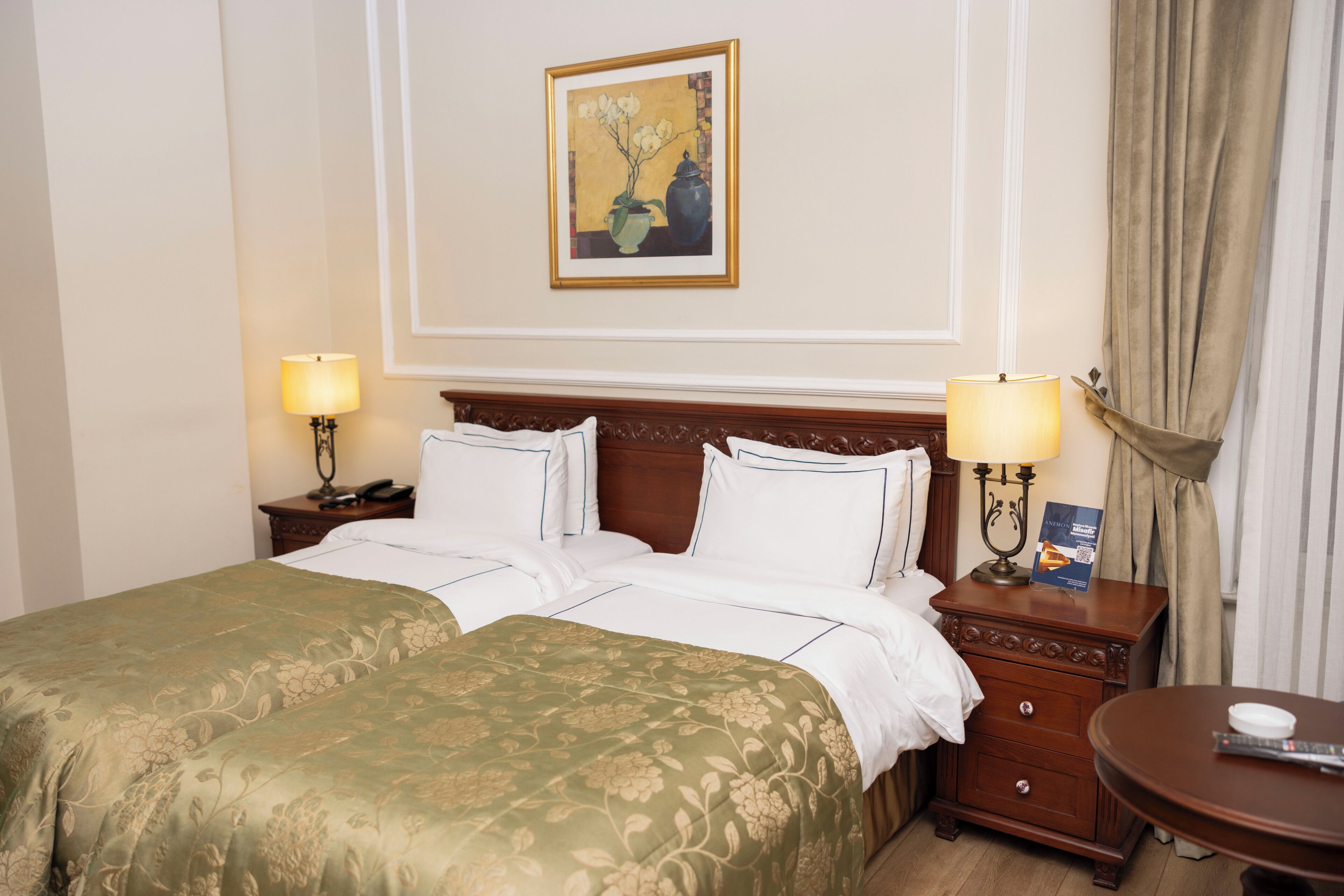 A hotel room with a double bed, two bedside tables, a nightstand, a lamp, a framed picture on the wall, and a small table with a remote control.